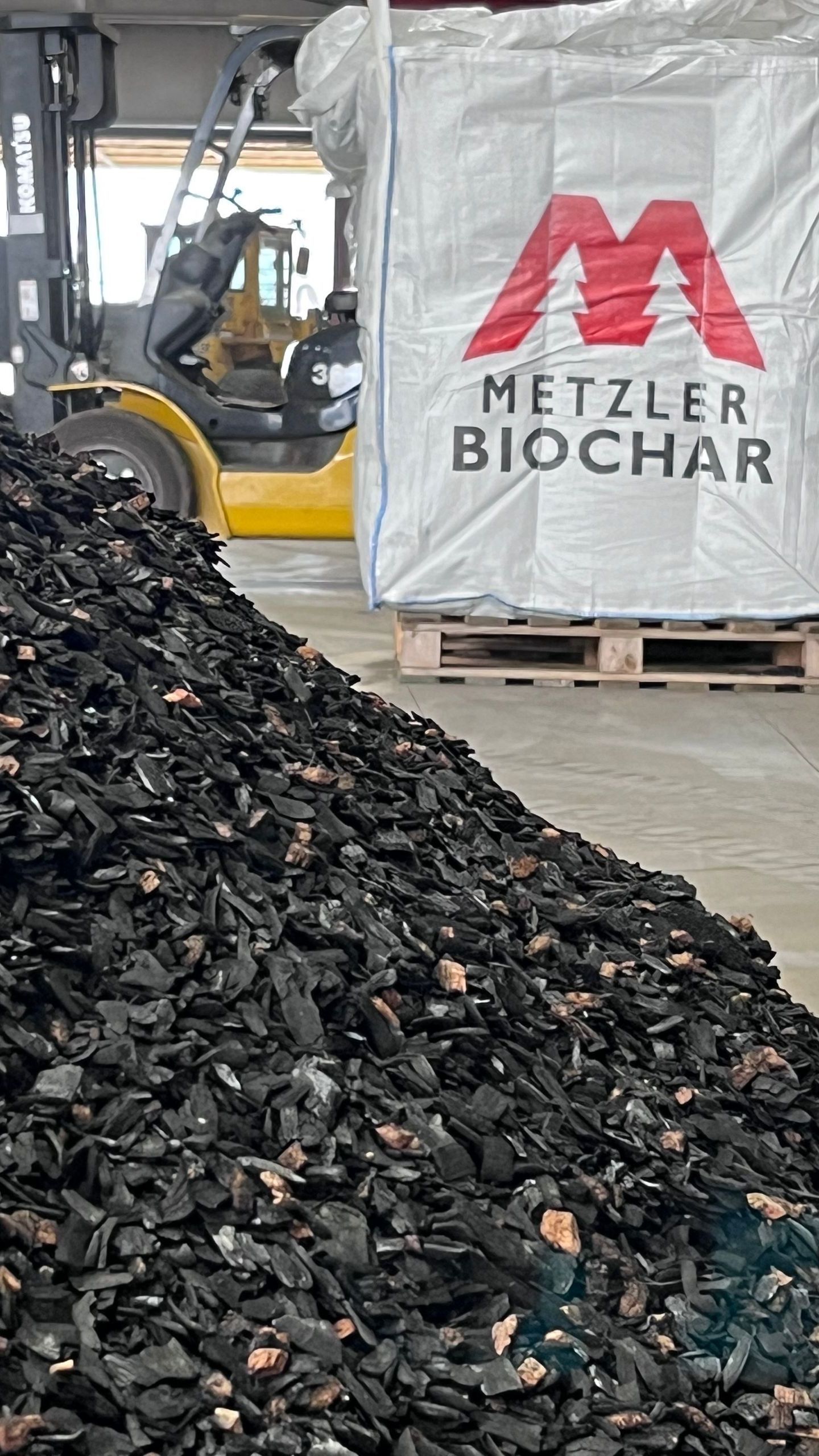 A large pile of metzler biochar is sitting next to a forklift.