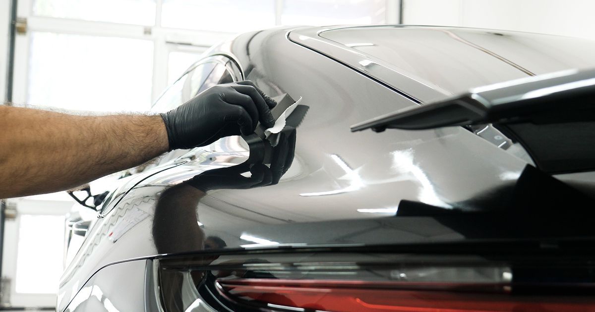 Gloved hand polishing the rear side of a silver car in a garage