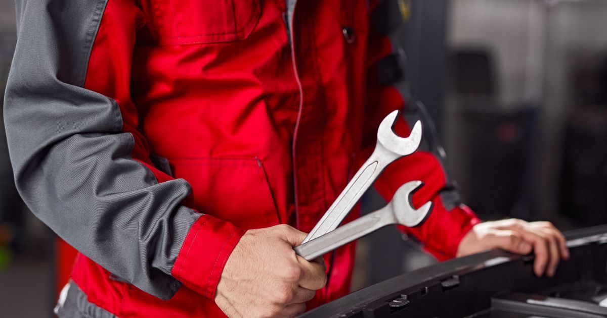 Mechanic in red vest holding wrenches beside a car engine