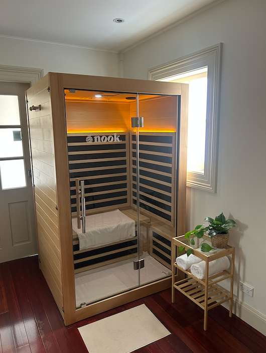 Wooden infrared sauna in a bright room, with warm interior lights and a small plant stand nearby — Burwood Back Pain in Strathfield, NSW