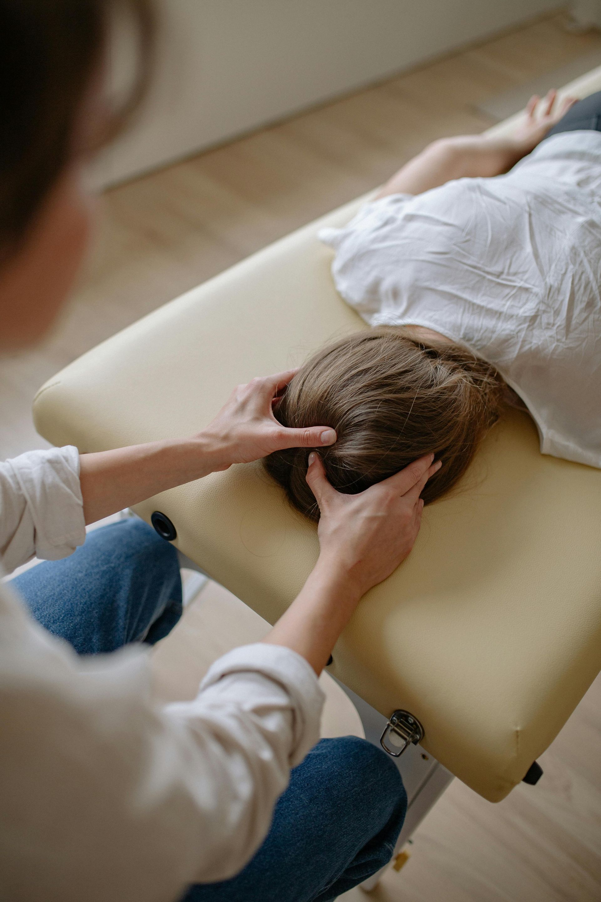 A Woman Is Giving a Child a Head Massage on A Table — Burwood Back Pain in Strathfield, NSW