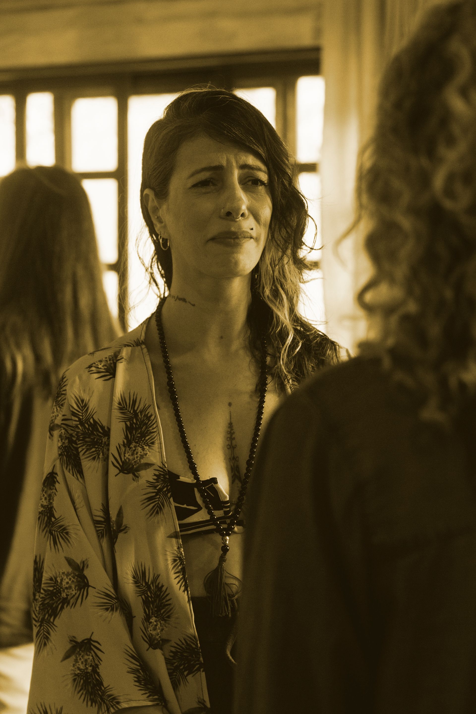 Mulher falando em uma sala com iluminação aconchegante, de frente para outras duas pessoas em primeiro plano.