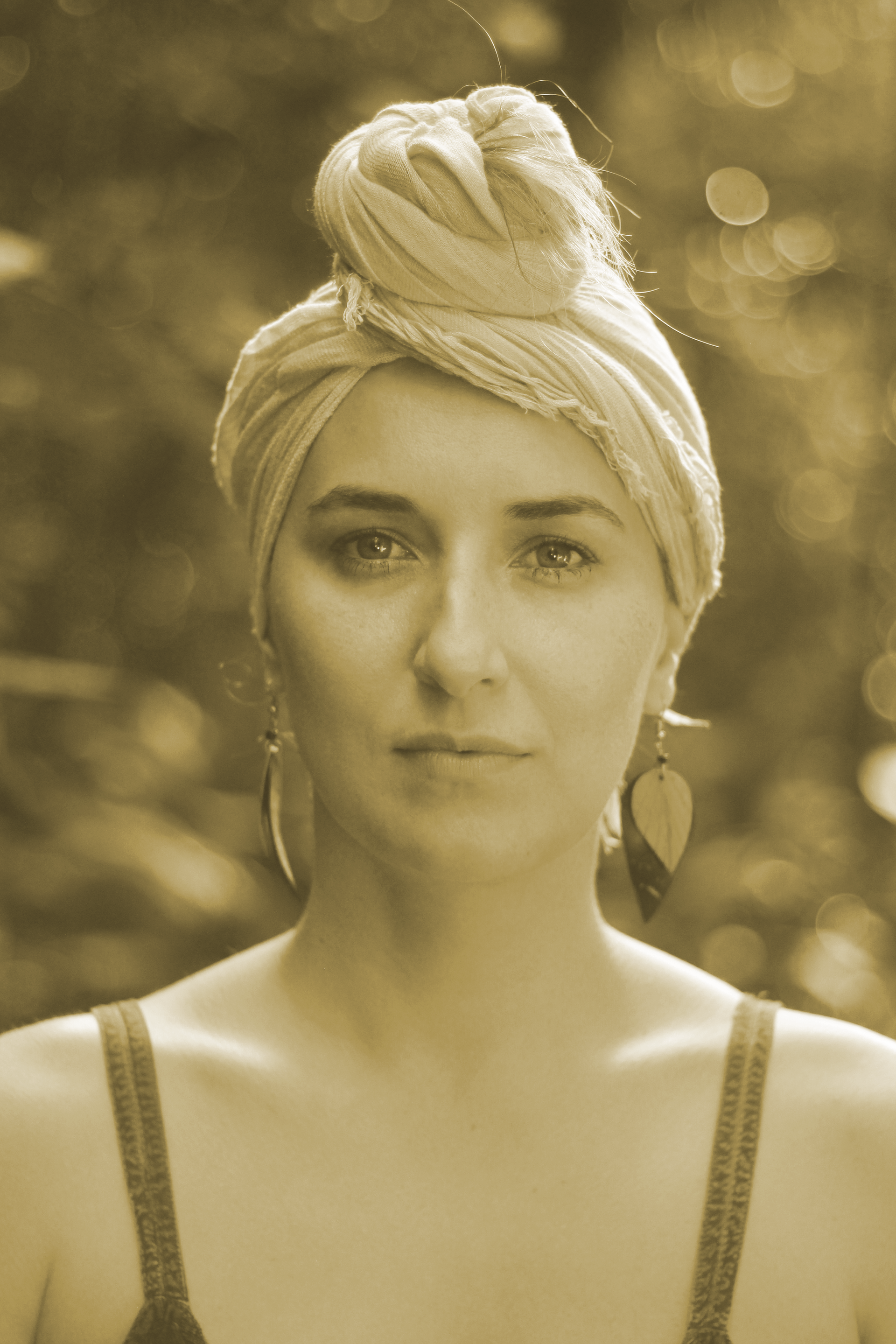 Retrato de uma mulher usando um lenço na cabeça, olhando para a frente contra um fundo suavemente desfocado.