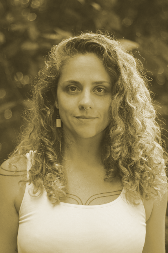 Retrato de uma mulher com cabelos cacheados e blusa branca contra um fundo externo desfocado.