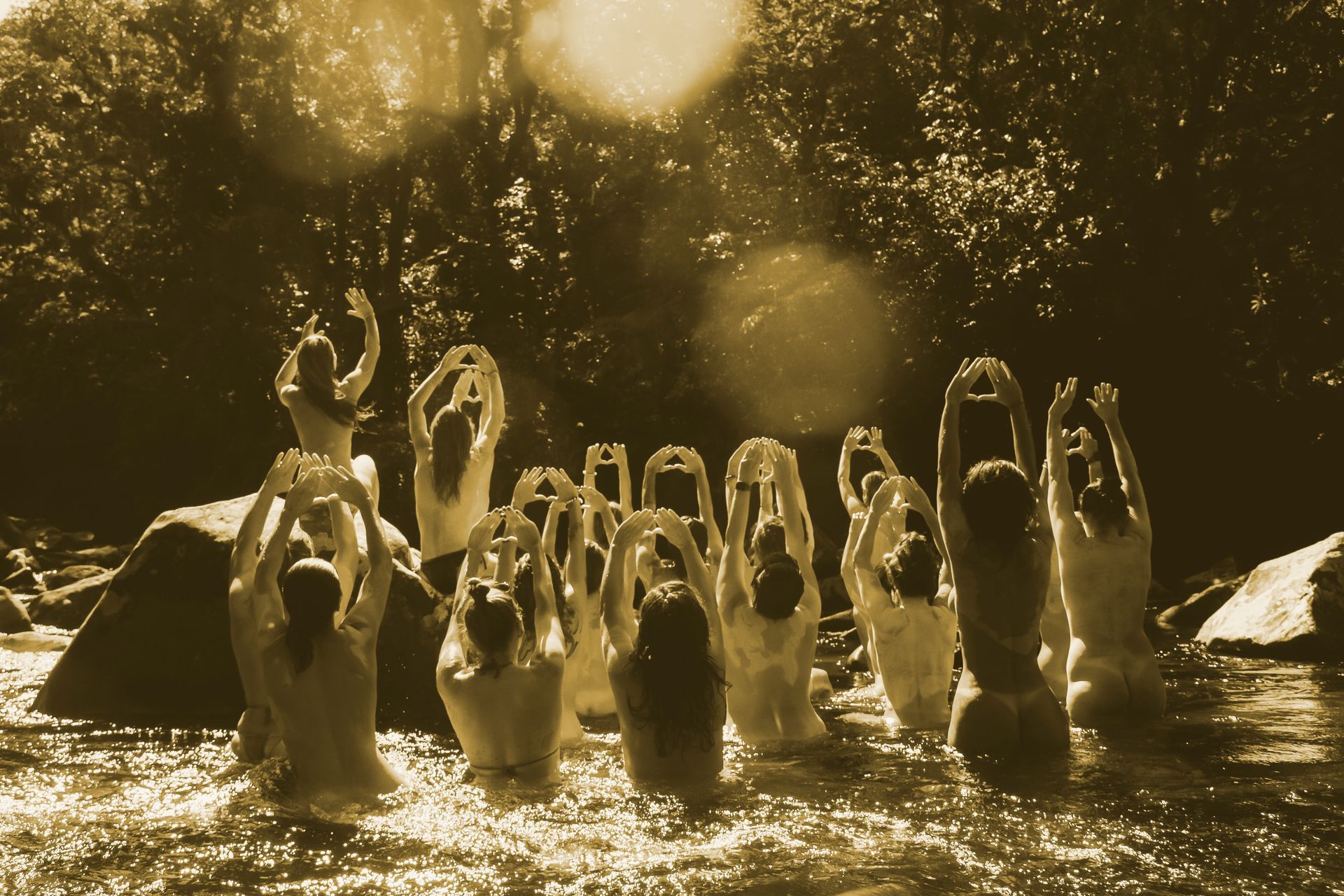 mulheres juntas em águas rasas, iluminados por trás pela luz quente do sol e pelas gotas que respingam.
