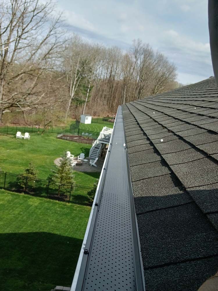 A gutter on the roof of a house with a view of a backyard.