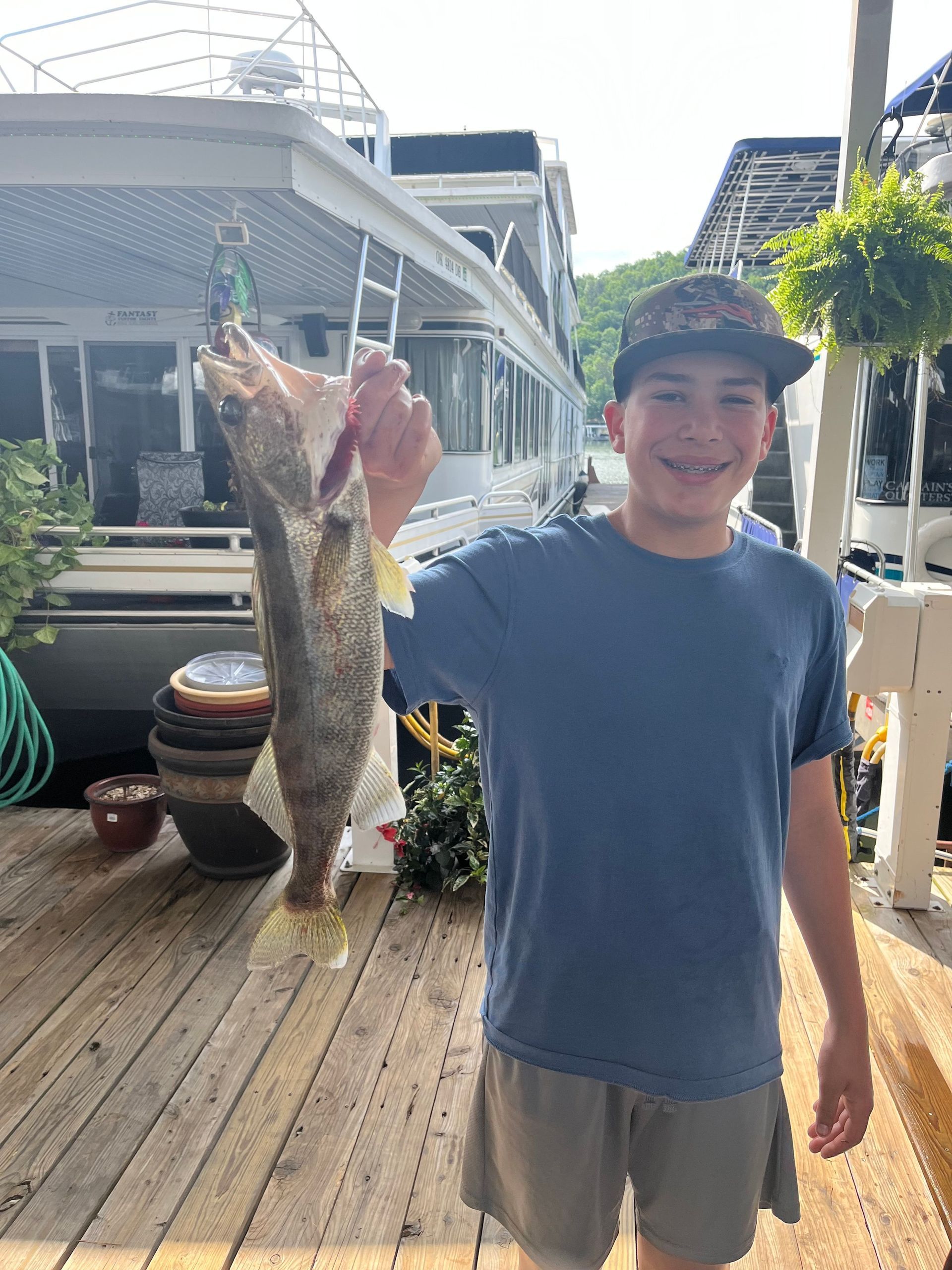 A young boy is holding a large fish on a dock.