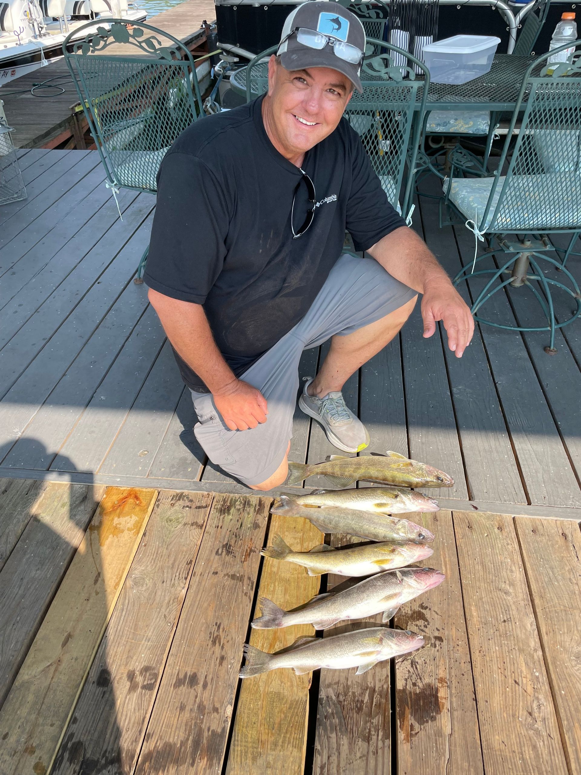 A man is kneeling down next to a pile of fish on a wooden deck.