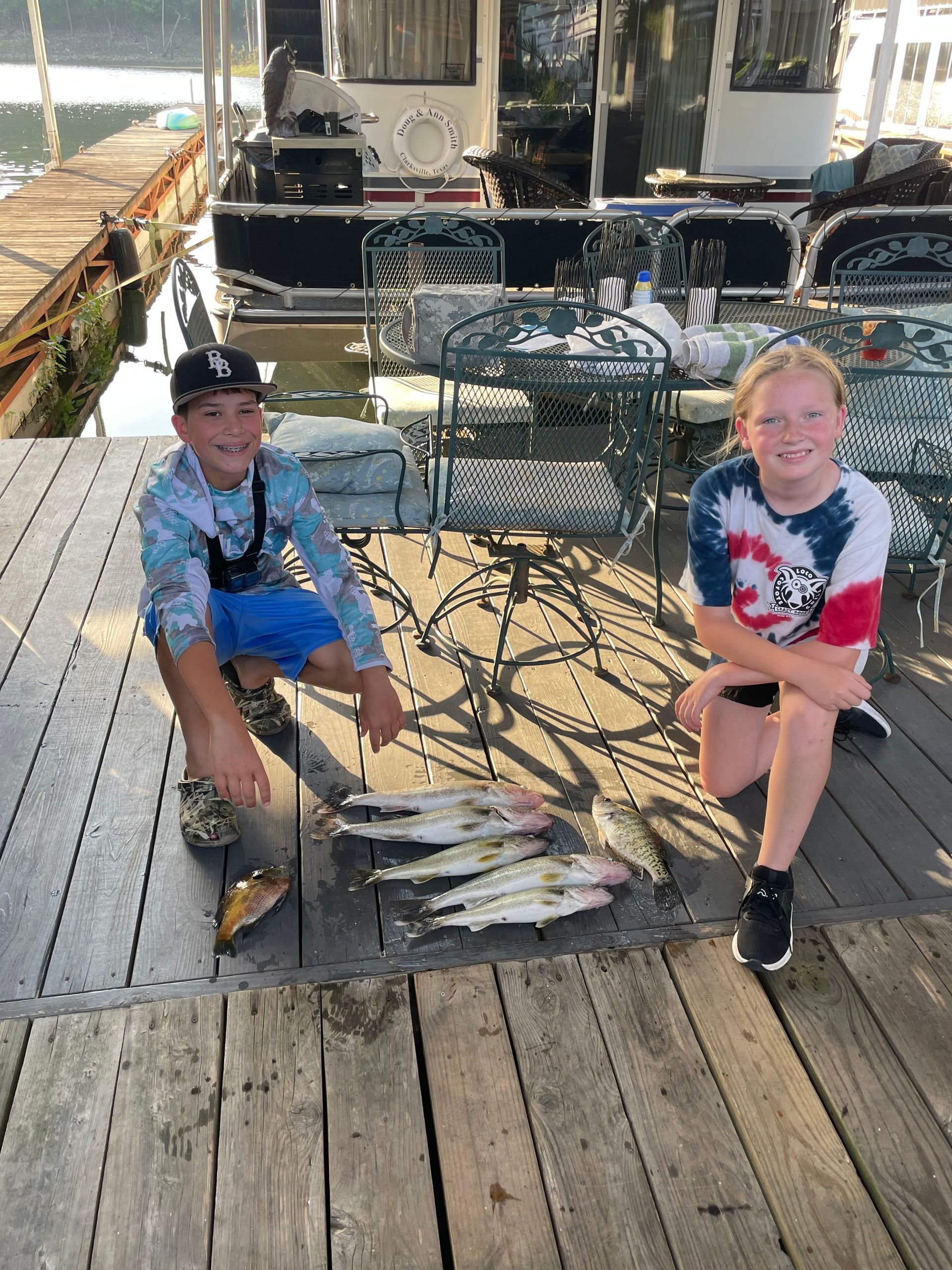 A boy and a girl are sitting on a dock holding fish.