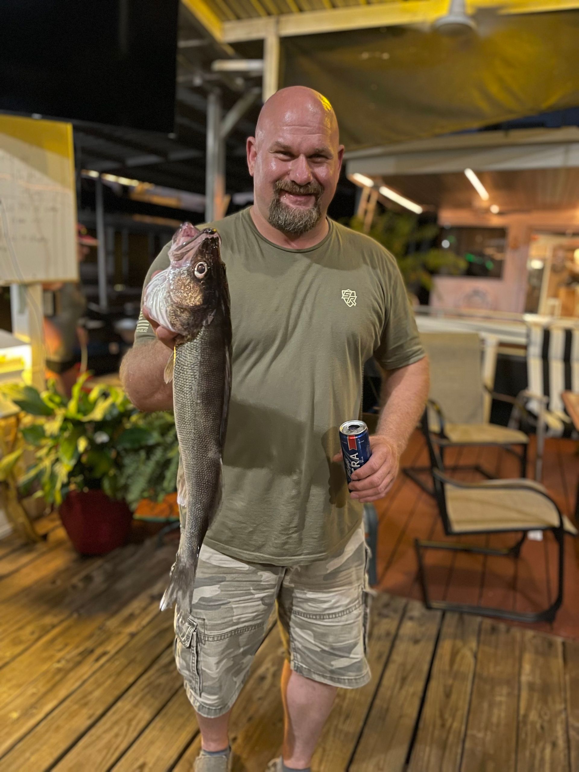 A man is holding a large fish and a can of pepsi.