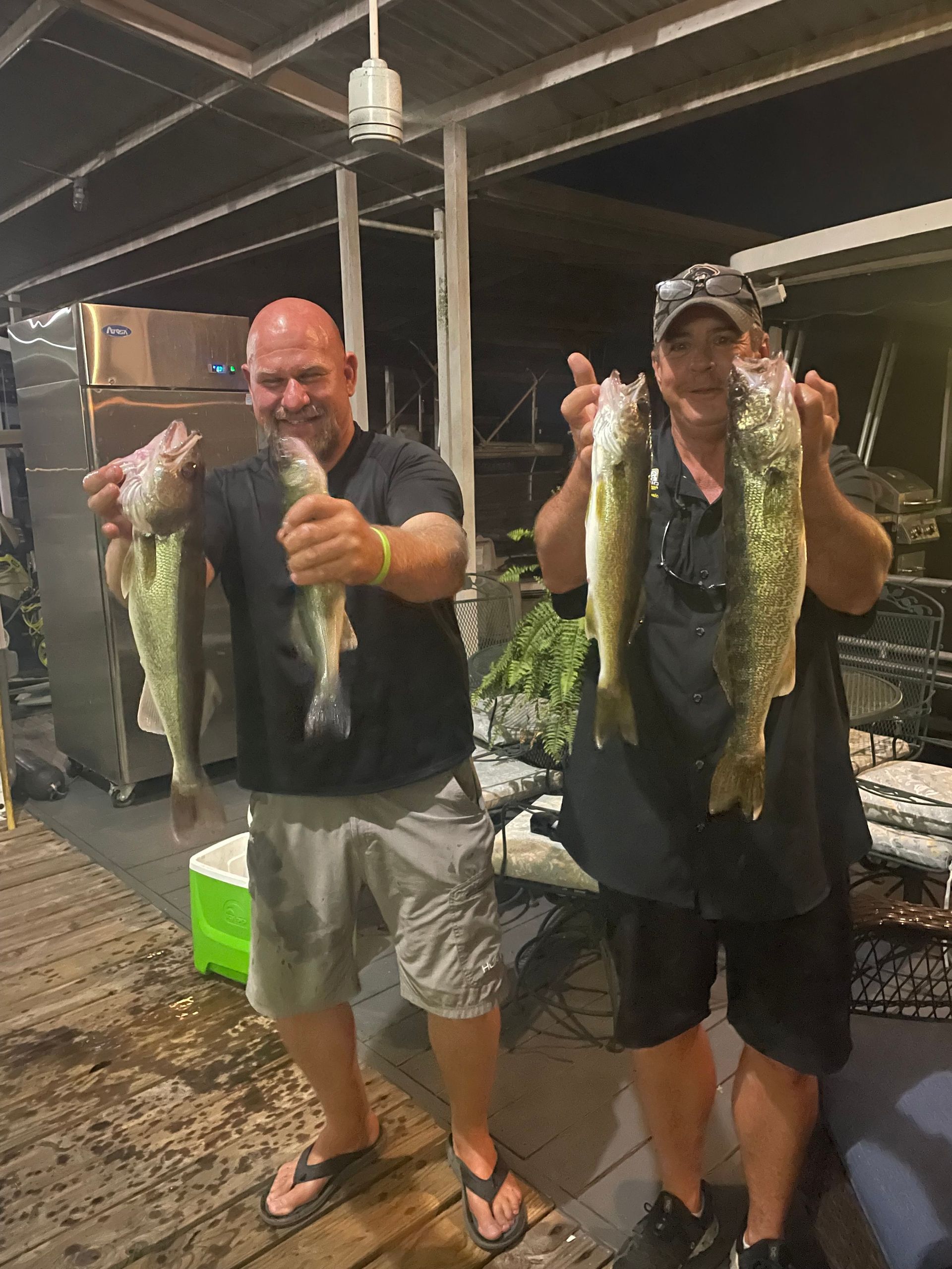 Two men are standing next to each other holding fish in their hands.