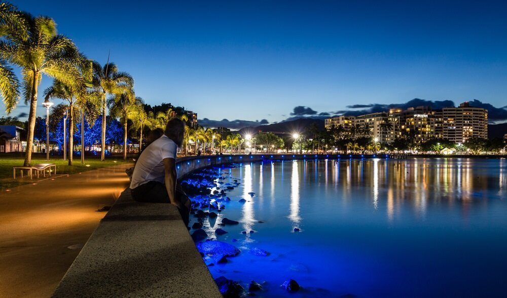 A Man Is Sitting On A Pier Overlooking A Body Of Water At Night — FNQ Freight & Logistics In Cairns, QLD
