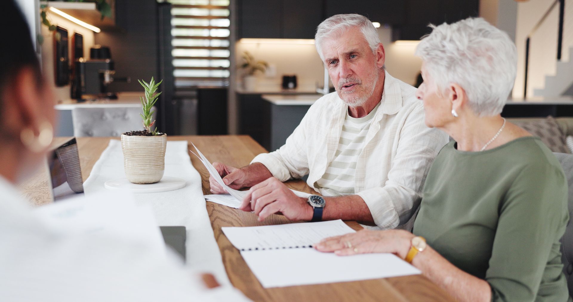 Two older adults reviewing documents with an advisor at a table in a modern home.