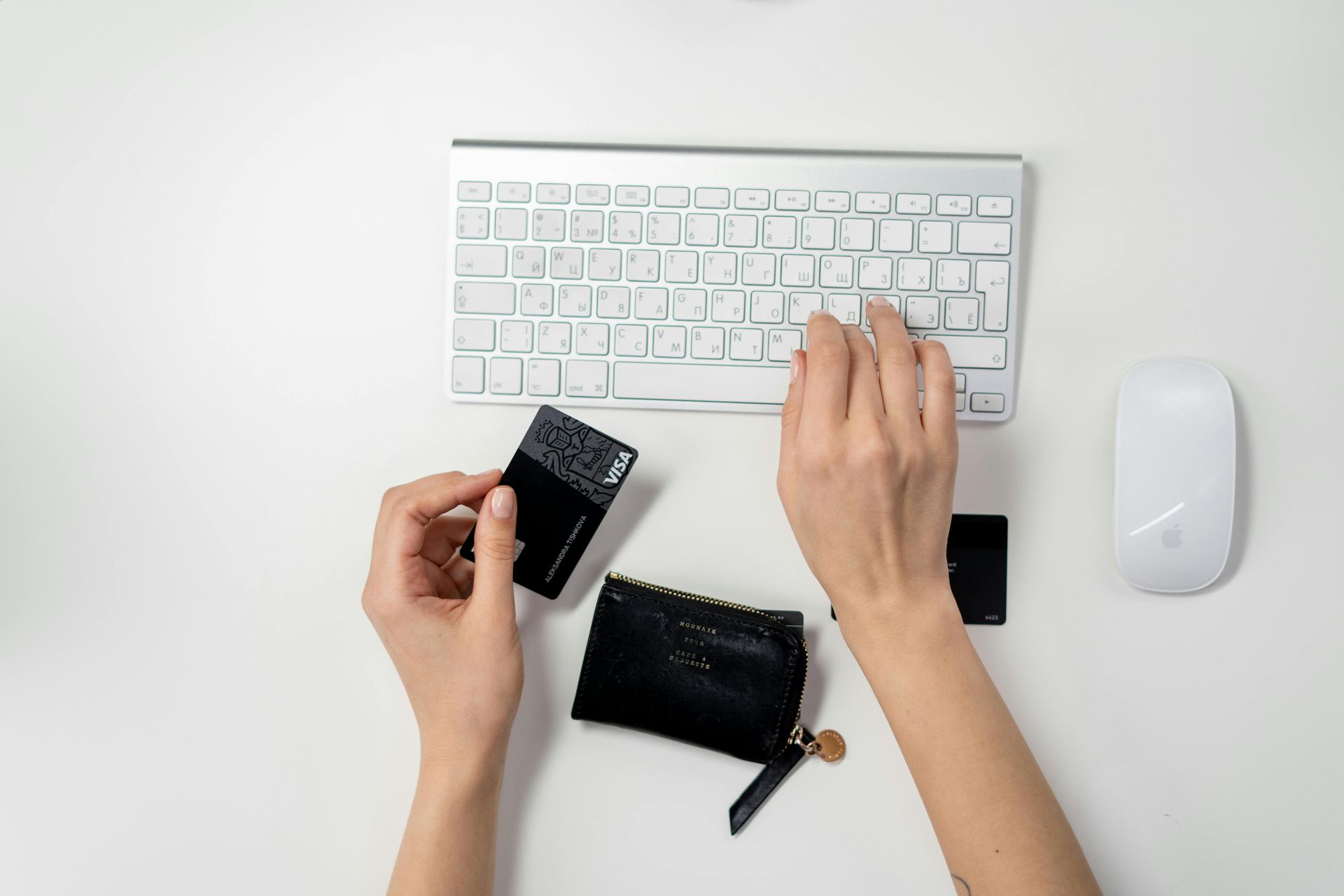 Hands using keyboard, credit card and wallet on white surface.