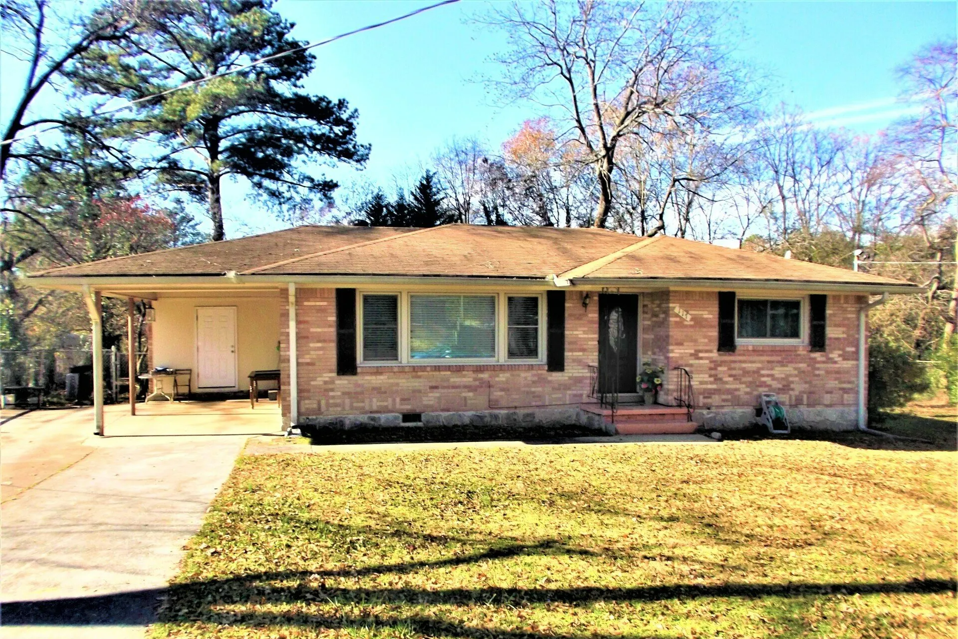 A brick house with a porch and trees in the background.