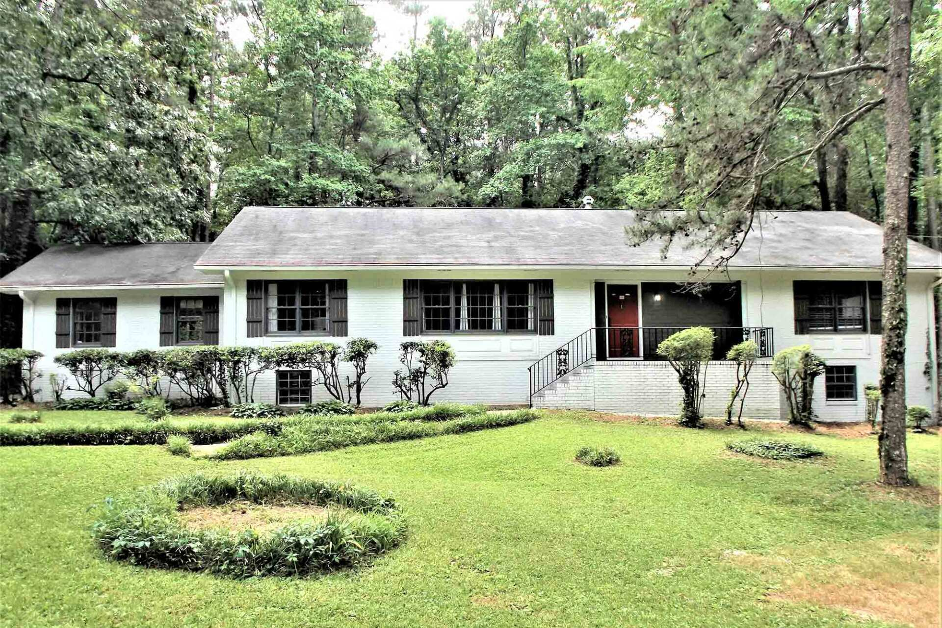 A white house with a circular garden in front of it surrounded by trees.