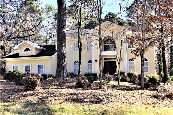 A large yellow house is surrounded by trees and grass.