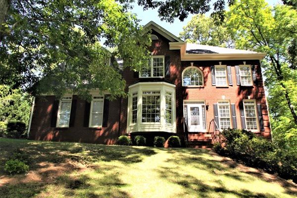 A large red brick house with white shutters is sitting on top of a lush green hill.