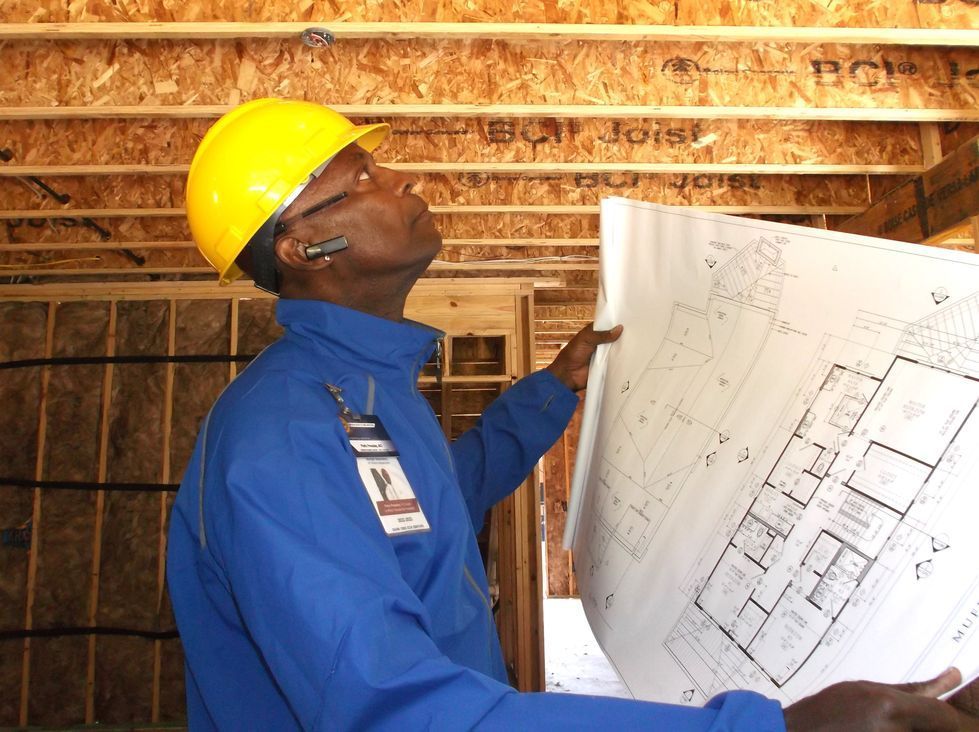 Construction worker in yellow hard hat reviewing blueprints inside a building frame