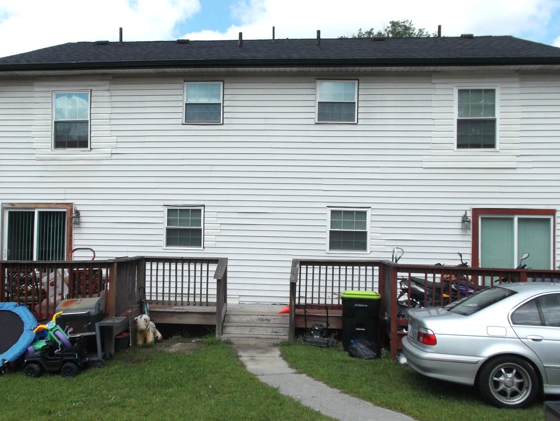 Back of a white two-story house with a small patio, lawn, and parked silver car