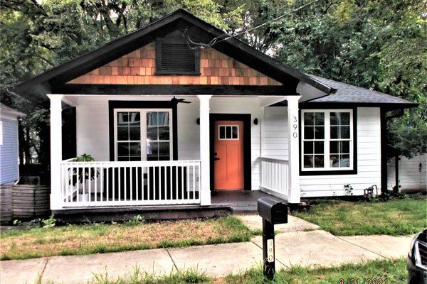 A small white house with an orange door and a porch.
