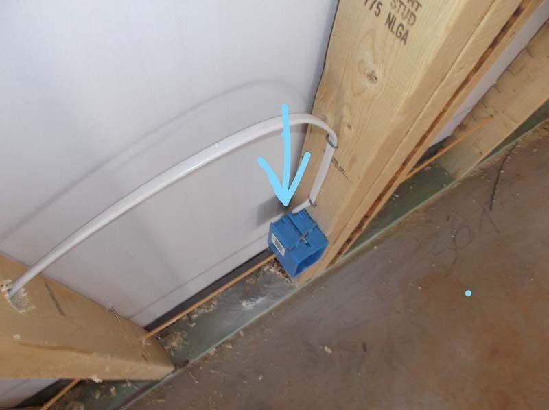 A blue box with a wire coming out of it is attached to a wall.