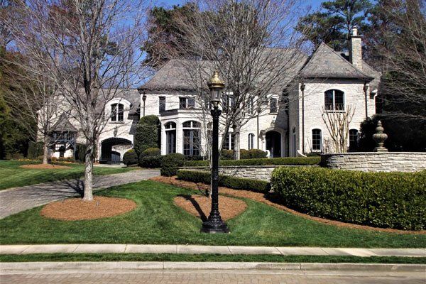 A large white house with a gray roof is surrounded by trees and bushes.