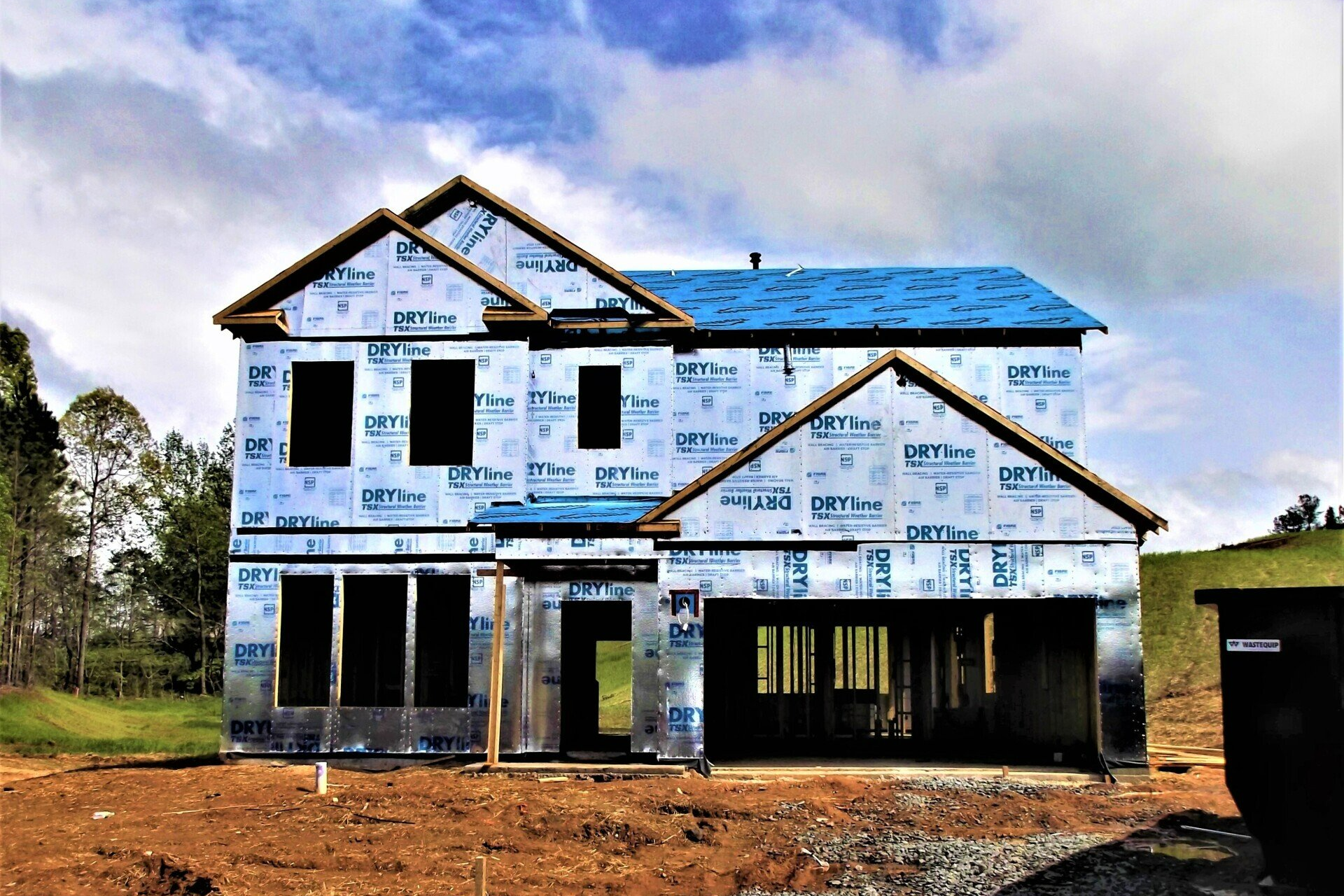 A house under construction with a blue roof and a dumpster in front of it.