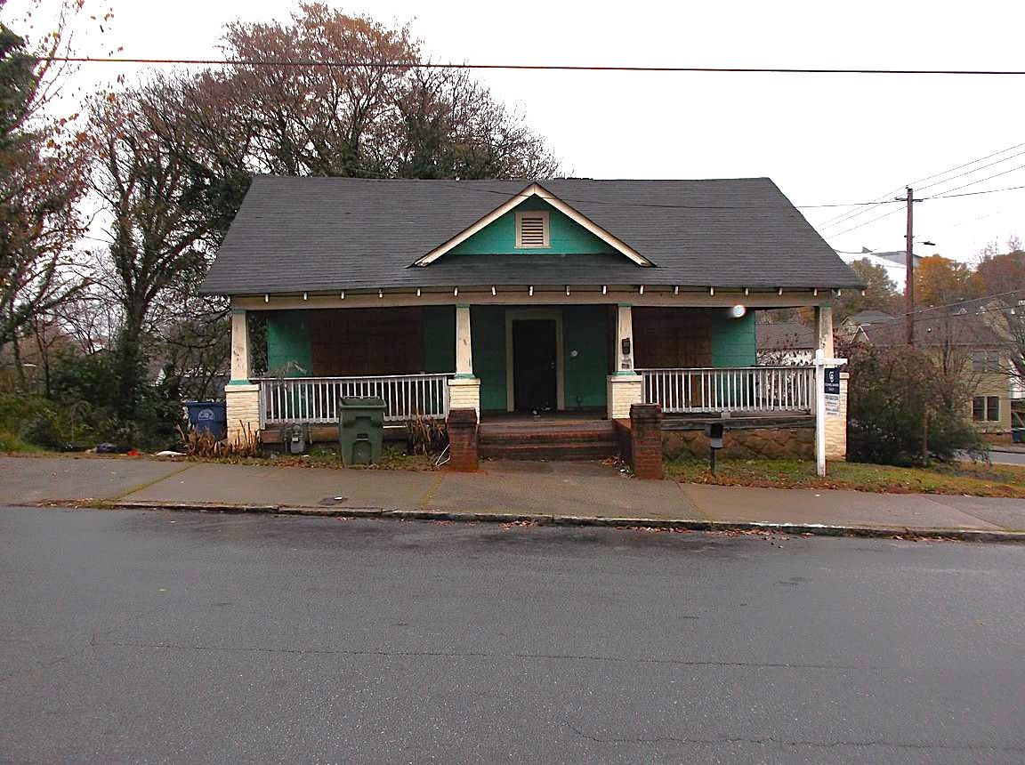 A small house with a porch is on the side of the road.