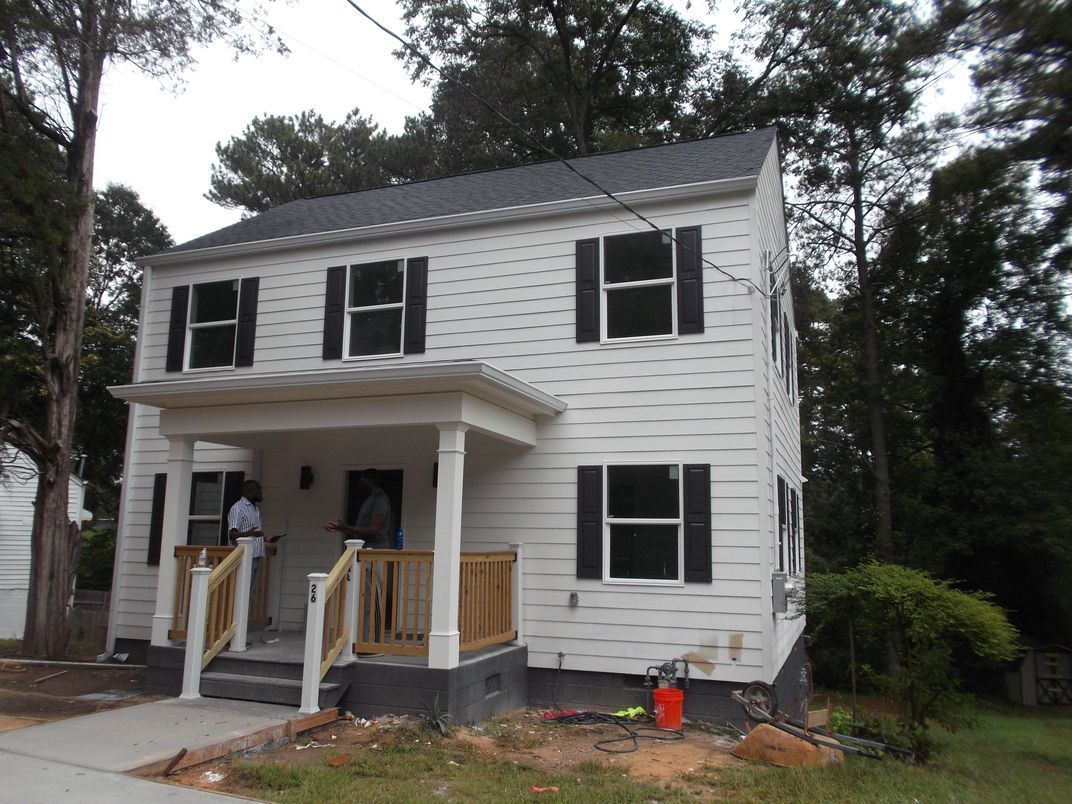 Two-story white house with black shutters and a small front porch under construction
