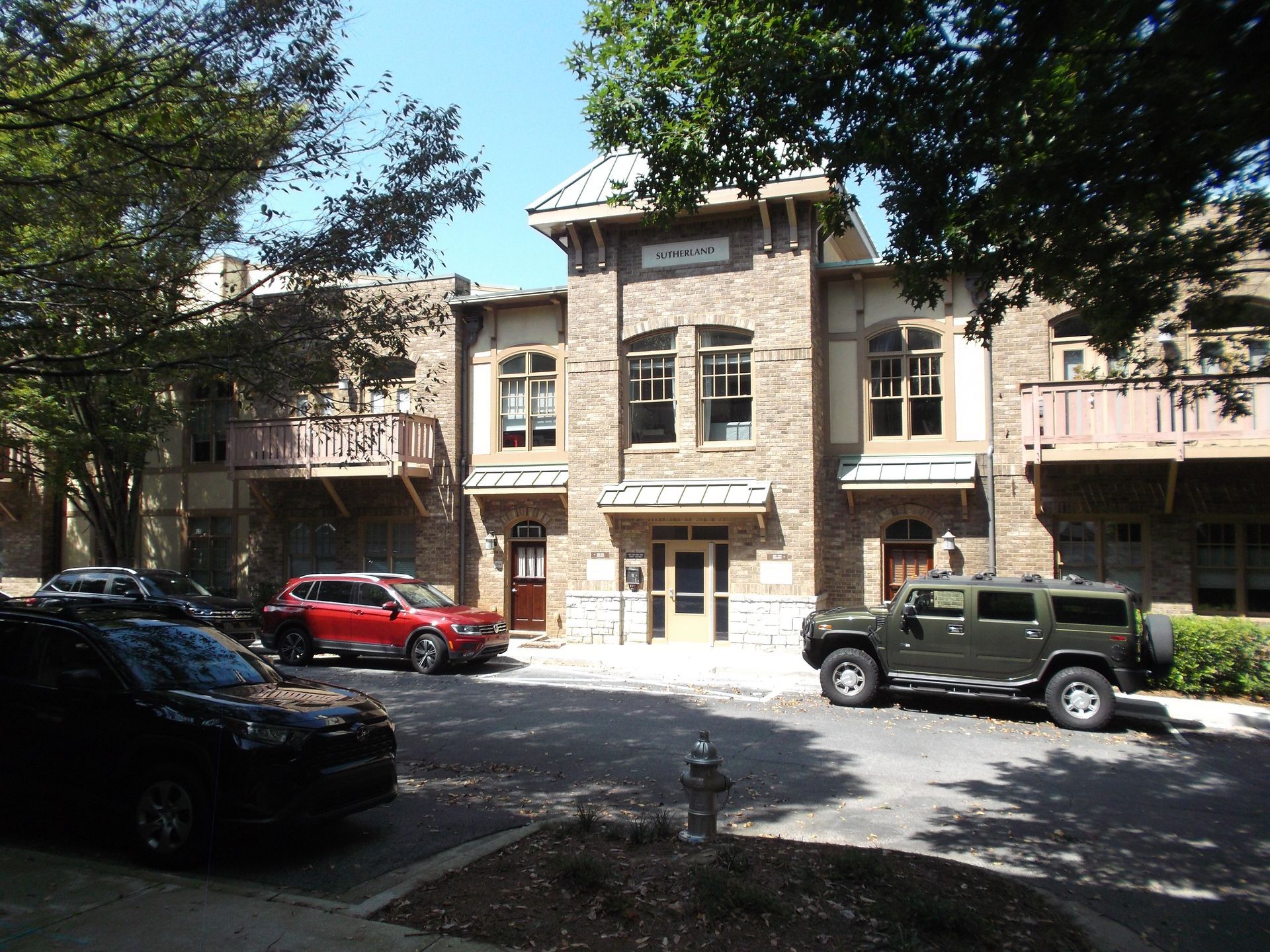 A stone building with a central entrance and parked cars in a sunny courtyard.