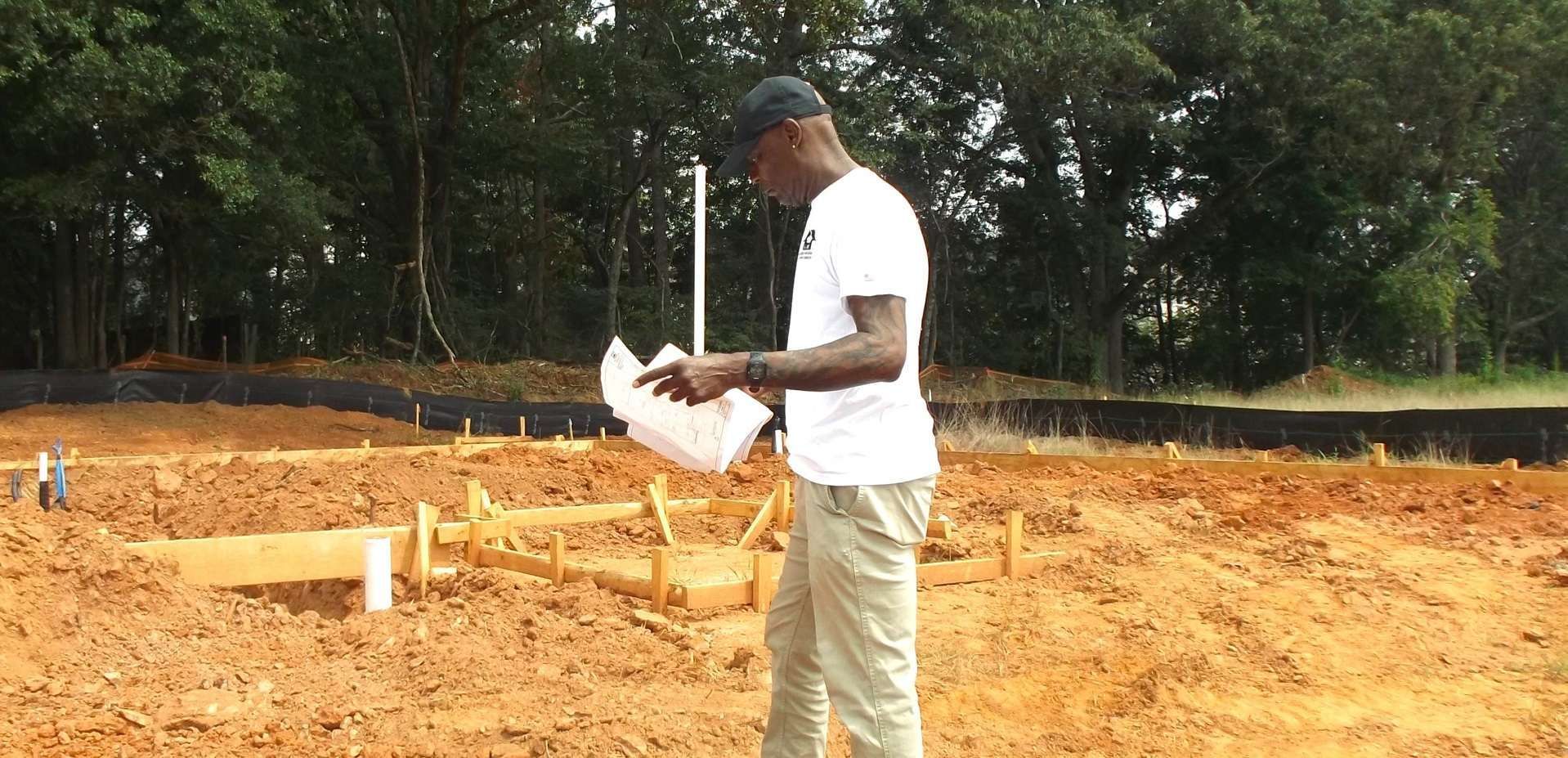 A man is standing in a dirt field holding a piece of paper.
