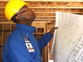 A man wearing a hard hat is looking at a blueprint