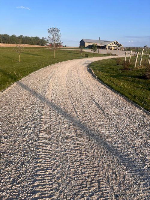 Gravel path curving through a green field toward a house under a clear blue sky
