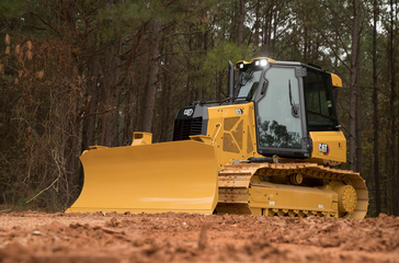Yellow bulldozer clearing dirt in a wooded area