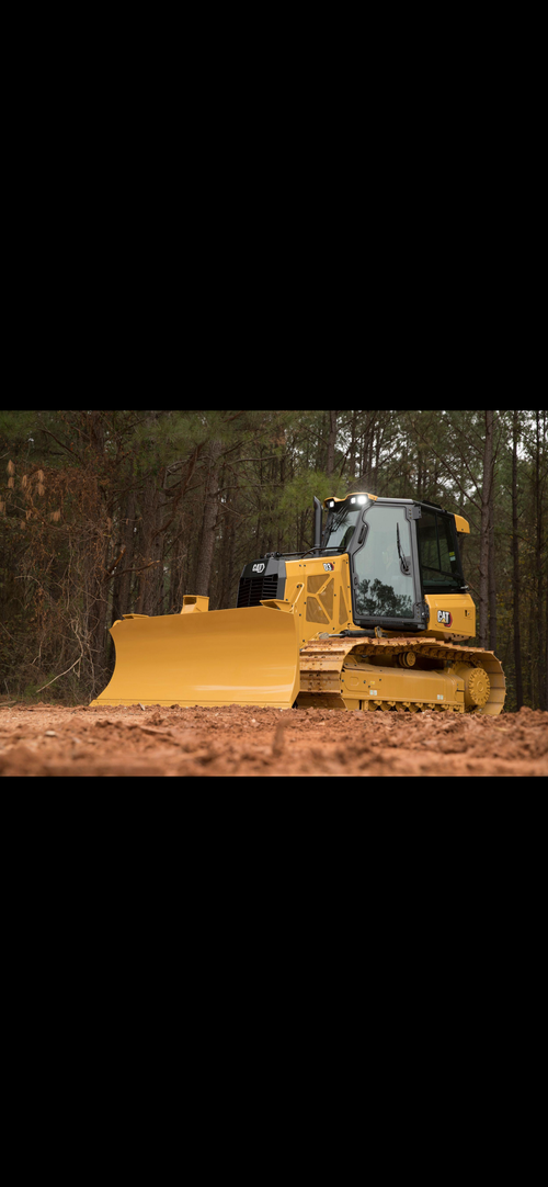 Yellow bulldozer pushing mud in a wooded area, with dirt flying around it.