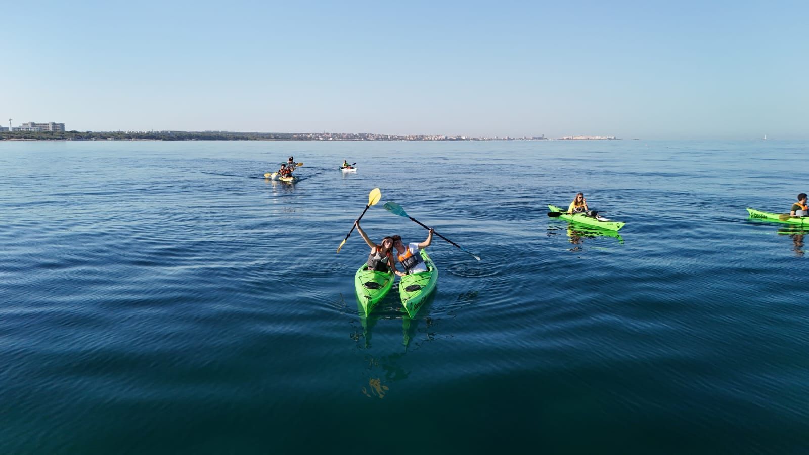 Kayakisti su imbarcazioni verdi e gialle remano su un calmo oceano blu vicino all'orizzonte