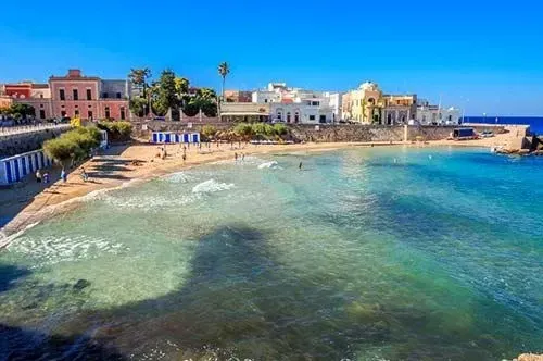 Villaggio costiero soleggiato con edifici color pastello e una tranquilla baia turchese sotto un cielo limpido