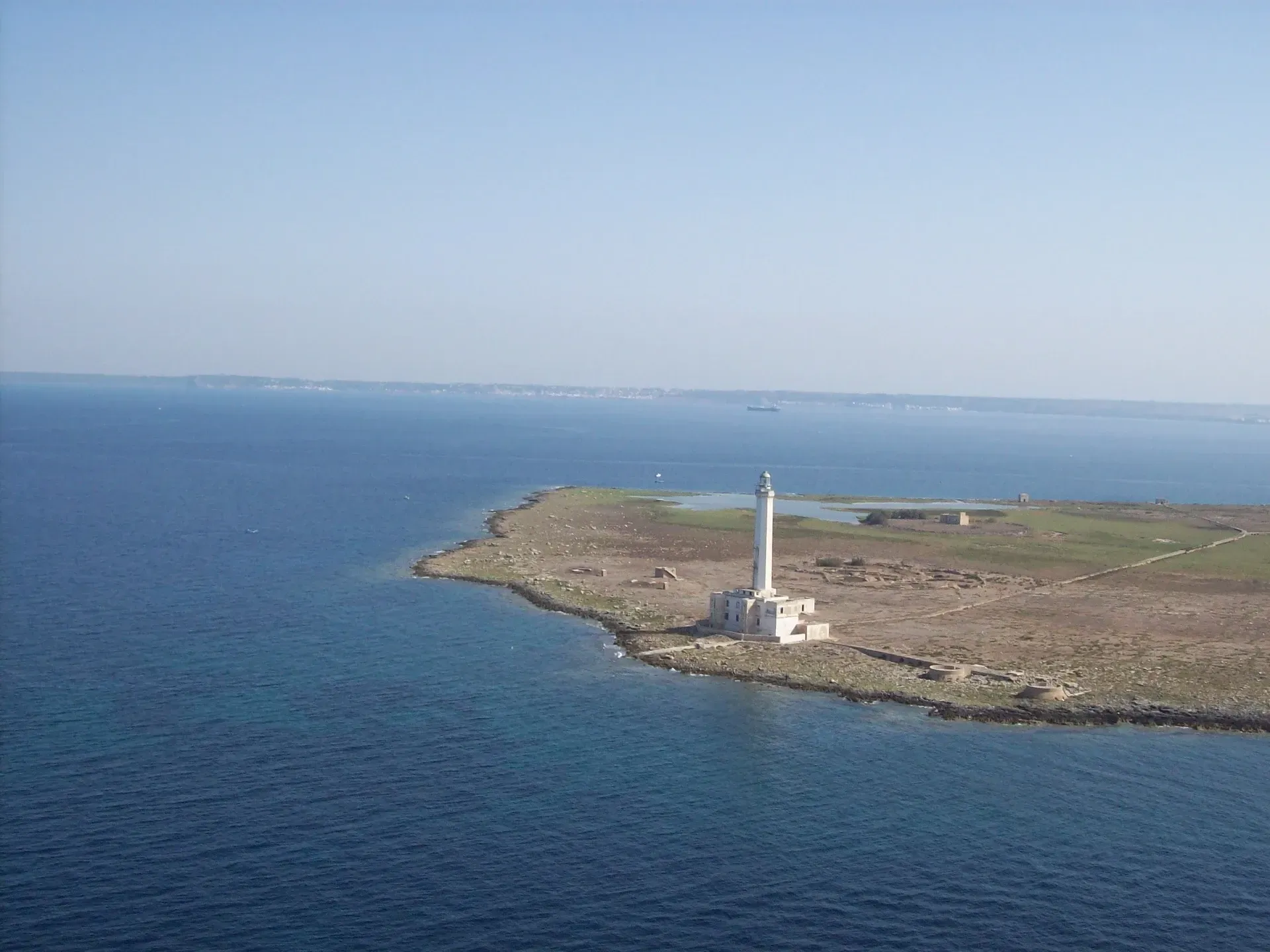 Un faro bianco su una costa rocciosa, accanto a acque di un blu intenso, sotto un cielo limpido.