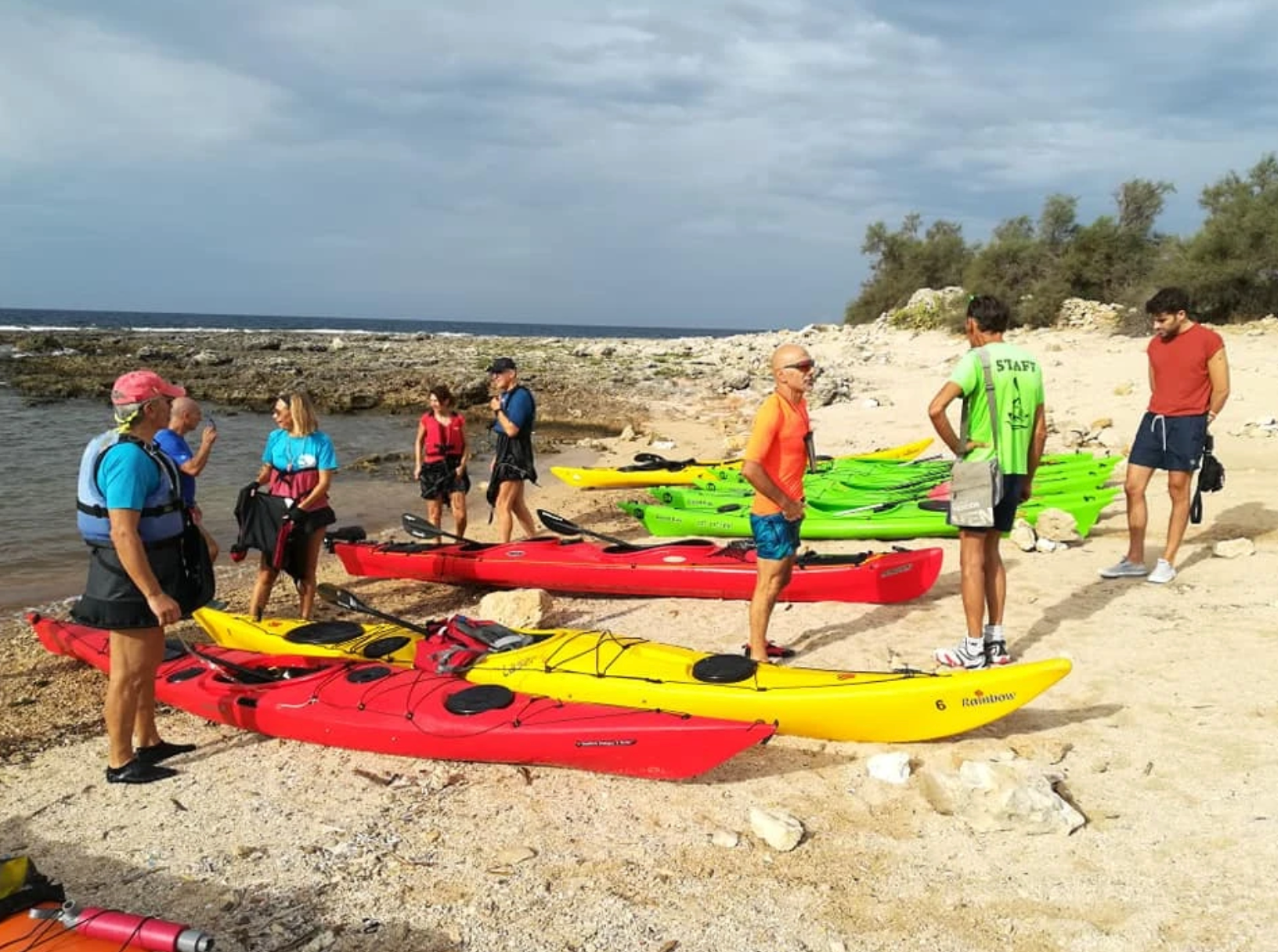 Persone che preparano kayak colorati su una spiaggia rocciosa in riva al mare