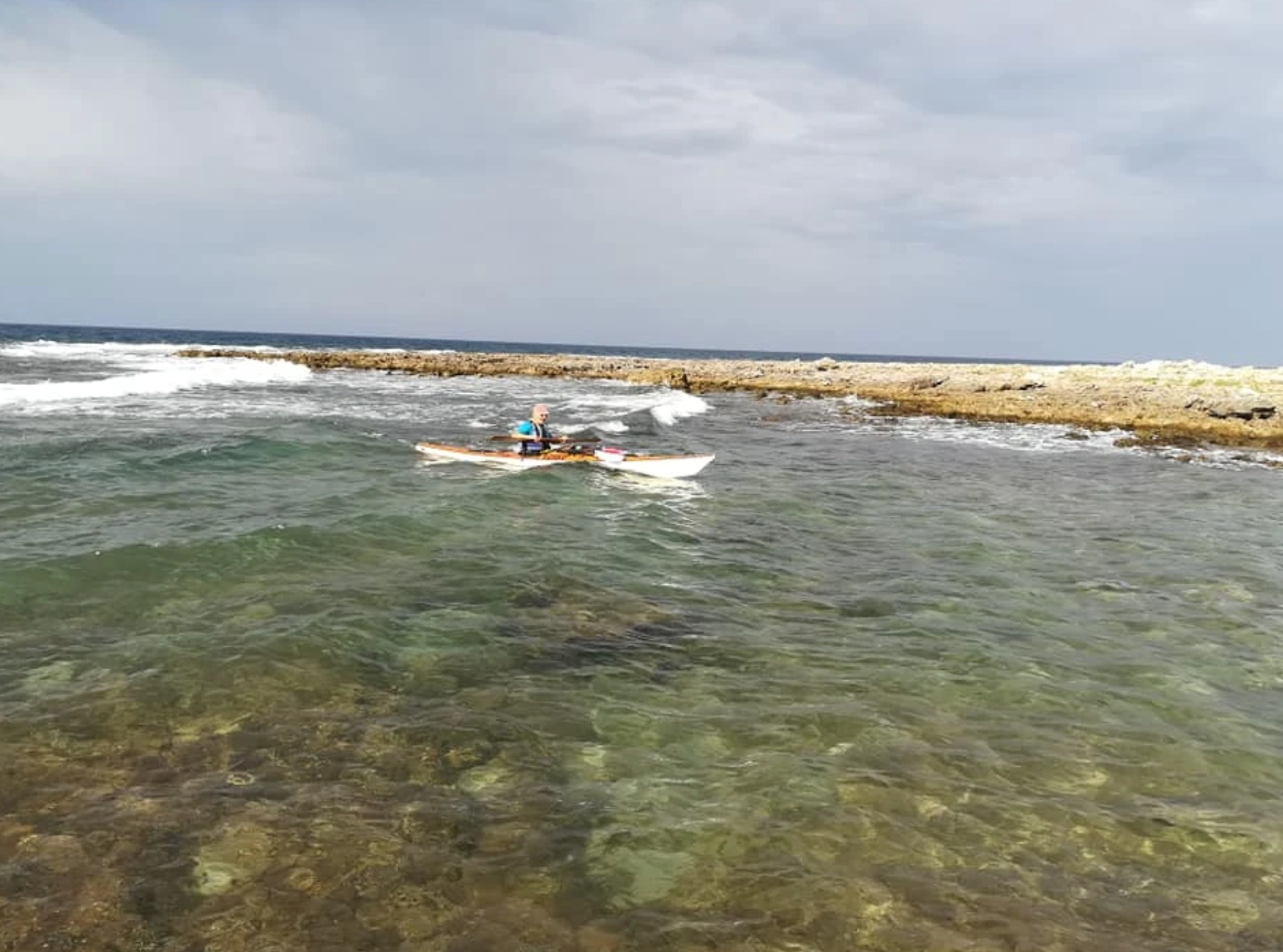 Una persona fa snorkeling in acque basse e limpide vicino a una barriera corallina rocciosa sotto un cielo nuvoloso.