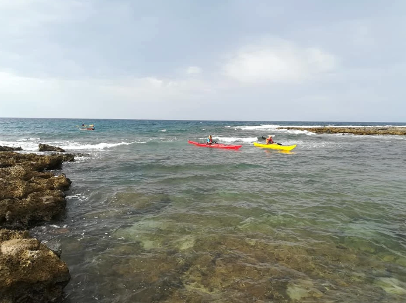Due kayak, uno rosso e uno giallo, su una tranquilla costa rocciosa con onde e mare aperto.