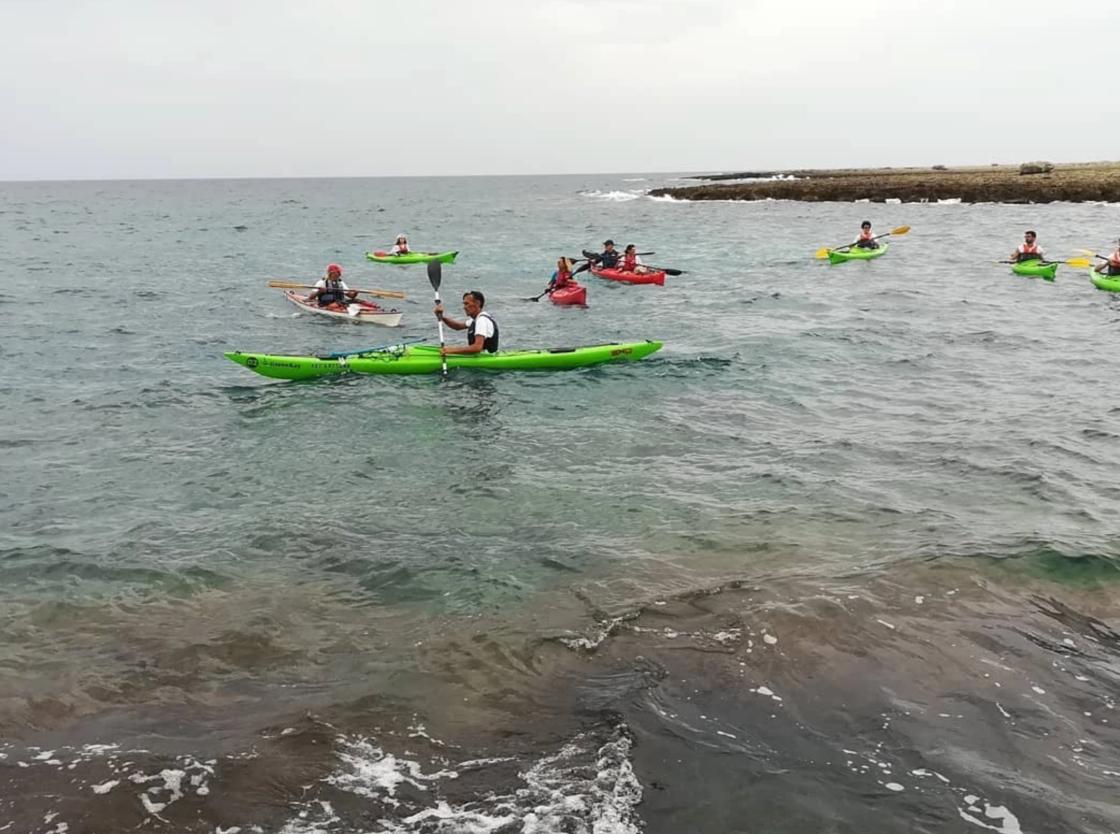 Persone in kayak su acque grigie e calme vicino a una costa rocciosa sotto un cielo nuvoloso.