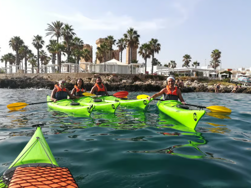 Persone in kayak su imbarcazioni verde brillante su acque calme vicino a una riva fiancheggiata da palme.