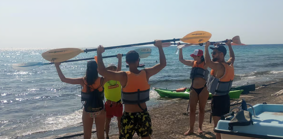 Quattro persone su una spiaggia assolata tengono le tavole da surf sopra la testa, in riva all'oceano.