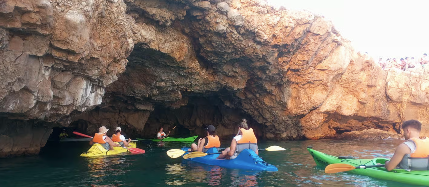 Kayakisti che pagaiano in una grotta marina rocciosa con acqua limpida e luce solare che filtra