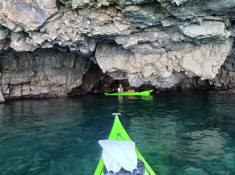 Due kayak verde neon su acque scure vicino all'ingresso roccioso di una grotta.