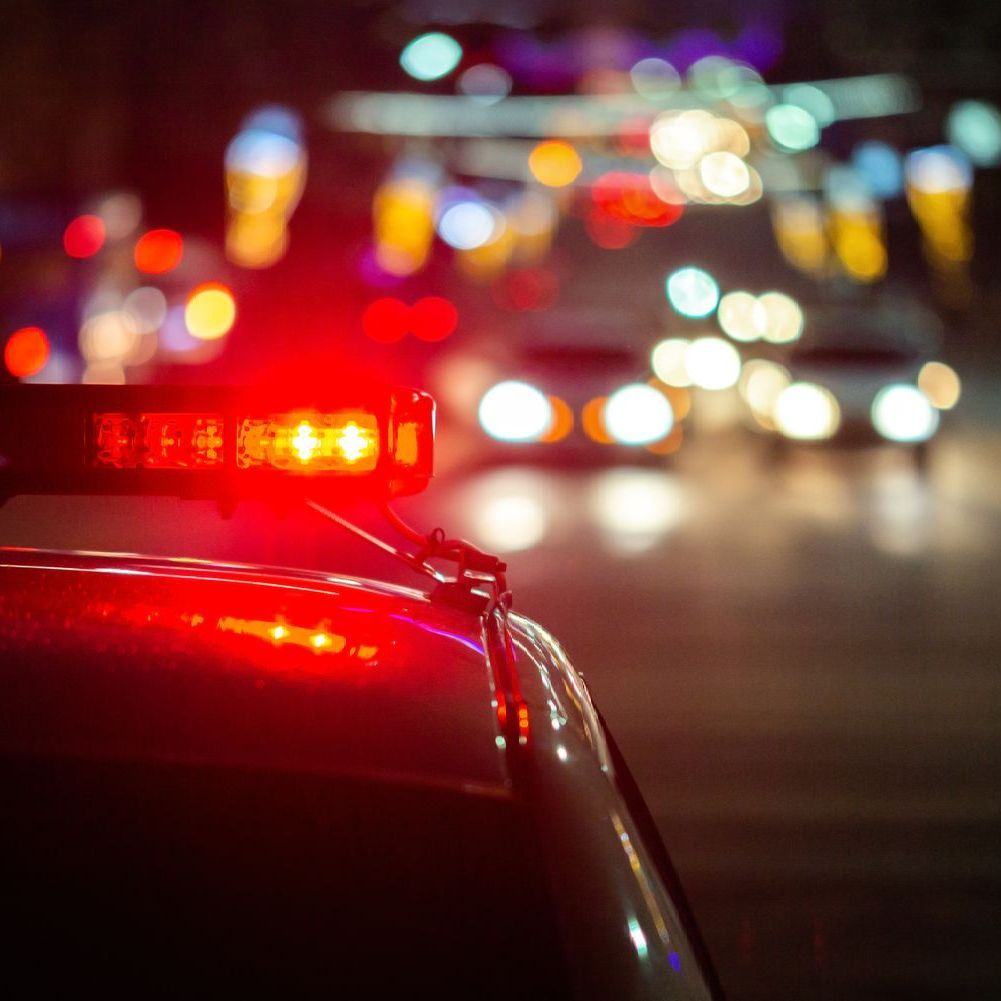 Police car with flashing red lights at night; blurry city lights in the background.