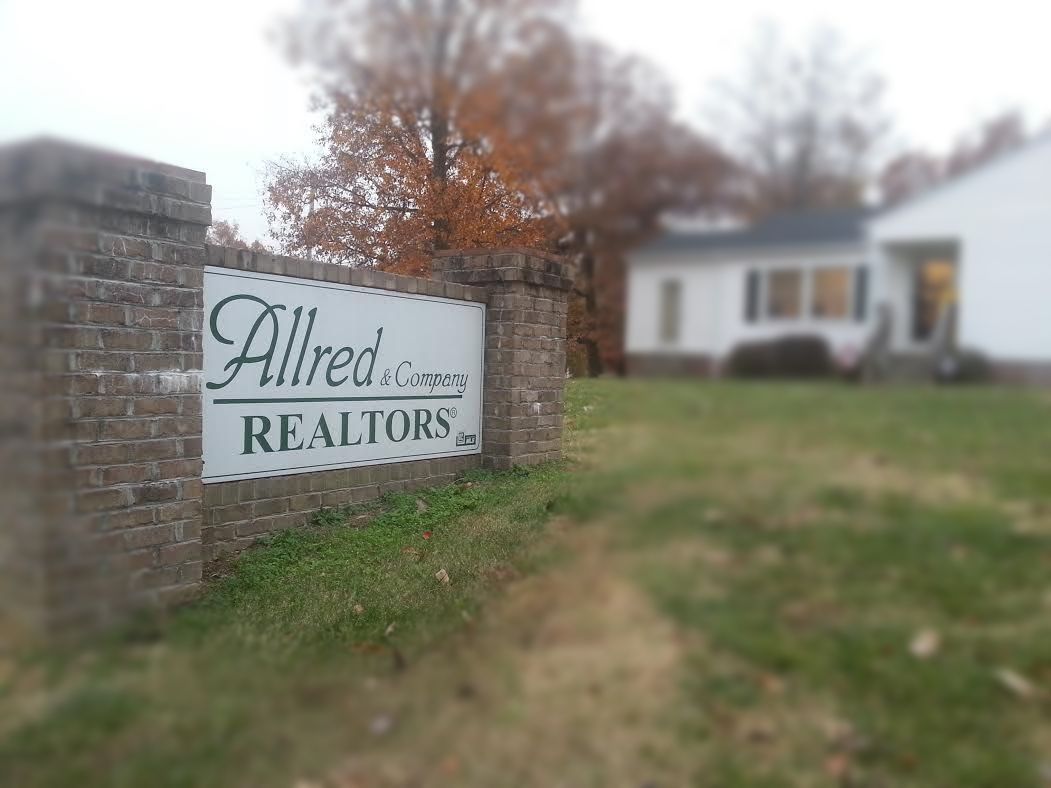 A sign for alfred realtors is on a brick wall in front of a house.