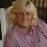 A woman is sitting in a chair wearing a pink shirt and smiling.